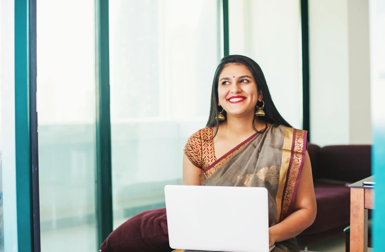 A woman in a sari working on a laptop while seated on a couch show to make money from home