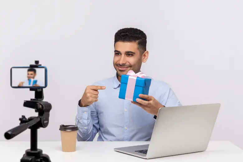 A man holding a gift box and a laptop with a camera, earning money in his free time