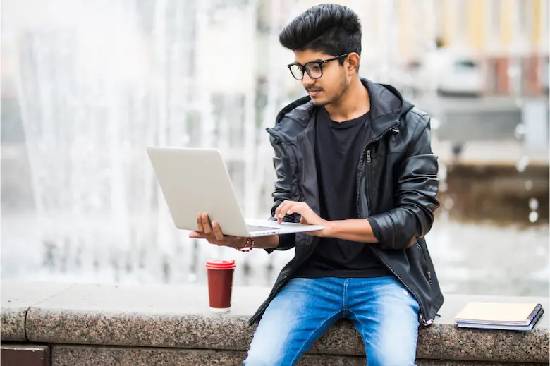 young boy in glasses sitting on a bench with a laptop