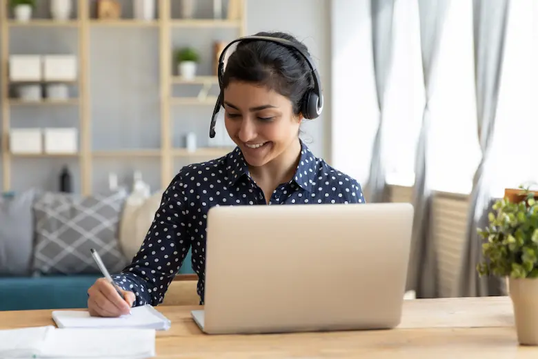 A woman headphones is focused on her laptop while working for best side hustle