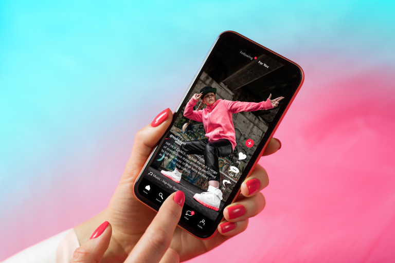  A person holding a smartphone with a video of a person dancing displayed on the screen. The smartphone has a red case and the background is blue and pink.
